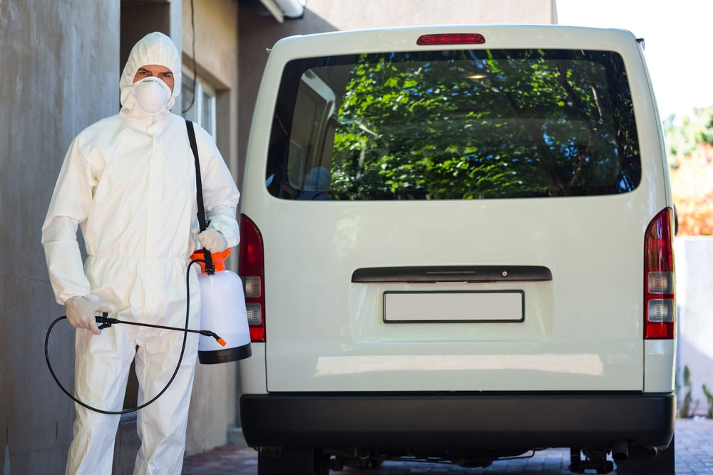 Pest control man in protective workwear standing behind a van